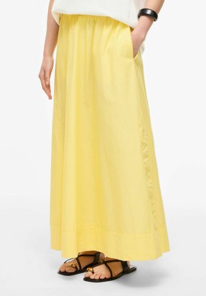 Kvinne iført gulstripet maxiskjørt med sidelomme, hvit topp, svarte sandaler med gull-accenter og svart armbånd.