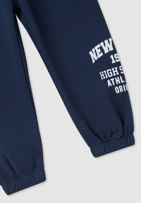 Granatowe spodnie dresowe wykonane z miękkiego materiału, z elastycznymi mankietami i białym nadrukiem: "NOWY JORK 1991 SPORTY SZKOLNE."