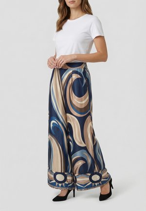 Femme portant un haut blanc à manches courtes et un pantalon large avec des motifs tourbillonnants bleus, beiges et marron, assorti à des talons hauts noirs.