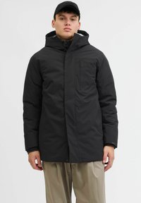 Sort isoleret jakke med høj krave, lynlås lukning, sidelommer og hætte. Slim fit, letvægtsstof med en mat tekstur.