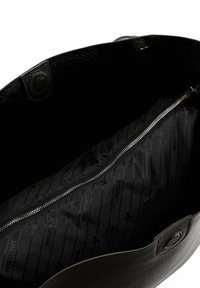 Innenseite einer schwarzen Ledertasche mit einem Reißverschlussfach und einem dunklen Stofffutter mit einem dezenten, sich wiederholenden Logo-Muster.