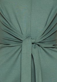 Gros plan sur un tissu bleu sarcelle noué, montrant la texture et les plis du matériau.