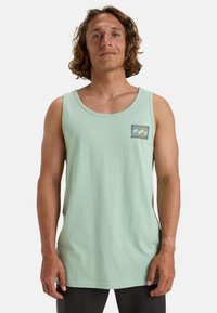 Pistaziengrünes Baumwoll-Tanktop mit einer quadratischen Tasche mit einem bunten Wellenmuster. Entworfen mit einem runden Ausschnitt und ärmellosem Schnitt.