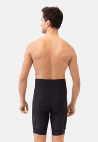 Shorts de cyclisme noirs avec rembourrage au niveau du siège et matériau extensible, dotés de deux poches latérales et d'une taille haute, conçus pour le confort et la mobilité.