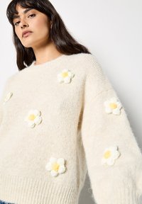 Maglione a maglia crema con vestibilità ampia, caratterizzato da fiori ricamati in bianco e giallo. Tessuto morbido e polsini a coste all'orlo.