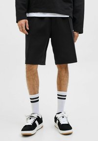 Shorts negri din bumbac, cu un croi relaxat, asociați cu șosete în dungi alb-negru și adidași negri cu accente albe.