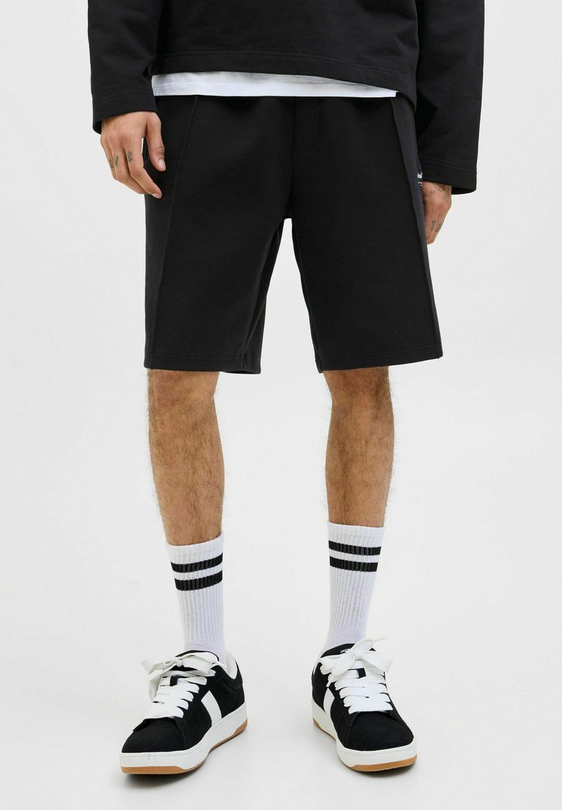 Sorte svedshorts med afslappet pasform, parret med hvid- og sort stribede sokker samt sorte sneakers med hvide detaljer.