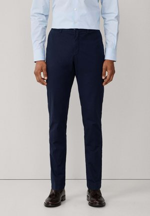 Pantalon bleu marine en tissu léger, à coupe droite, avec poches avant et texture lisse. Associé à des chaussures marron.