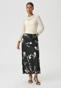 Haut à manches longues en dentelle crème associé à une jupe maxi en satin noir à motifs floraux. La tenue présente des motifs floraux délicats et des talons aiguilles noirs à lanières.