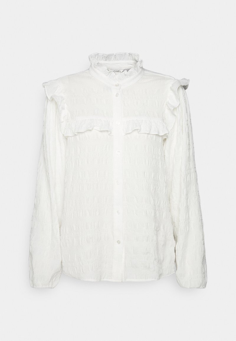 Blouse blanche texturée à manches longues avec fermeture boutonnée devant, col montant à volants et détail à volants sur la poitrine et les coutures des épaules.