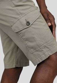 Shorts cargo beiges en tissu texturé, dotés de poches frontales avec fermetures à bouton et de détails cousus le long des ourlets.