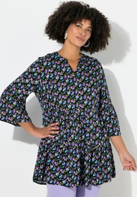 Sort tunika med et blomsterprint featuring lilla og blå blomster, V-hals, trekvartlange ærmer og en lagdelt flæsekant.