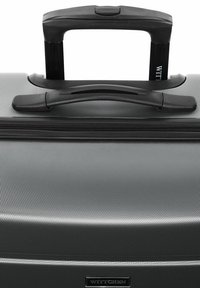 Gray wheeled suitcase with a textured surface, black handle, and zipper detailing. Features logo plate on the front.