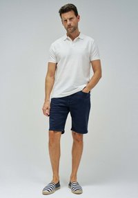 Camisa polo blanca texturada, pantalones cortos navy y alpargatas a rayas. La polo tiene mangas cortas y los pantalones cortos son hasta las rodillas.