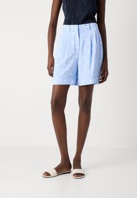 Light blue shorts with white polka dots, pleated design, and cuffed hems. Paired with beige flat sandals.