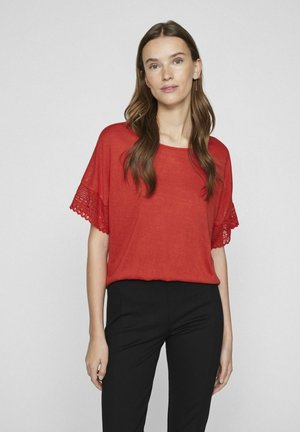 Top corto rojo de manga corta con borde de encaje abierto en las mangas, de corte holgado y cuello redondo, combinado con pantalones negros. Textura suave.