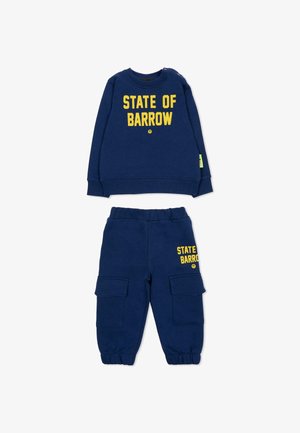 Navyblauwe sweatshirt met "STATE OF BARROW" in gele letters, gecombineerd met bijpassende cargopantalons met twee zijzakken. Zacht materiaal.