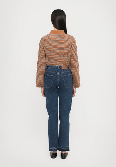 Λωρίδες μπλούζα μακρυμάνικη σε καφέ και πορτοκαλί, συνδυασμένη με ψηλόμεσα σκούρα μπλε τζην παντελόνια με πίσω τσέπες και ξεθωριασμένο τελείωμα.