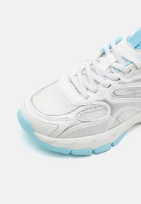 Baskets blanches avec des accents en maille et en cuir, détails bleu clair, semelle texturée et corps rembourré. Présente des lacets et un design de panneau latéral.