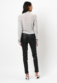 Grijze, fluffy trui met lange mouwen, gecombineerd met zwarte, strakke leren broek. De outfit heeft een cropped zoom en een slanke uitstraling.