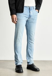 Světle modré džíny s úzkým střihem, které mají klasický design s pěti kapsami a jemným vyblednutím. V kombinaci s černými koženými botami.