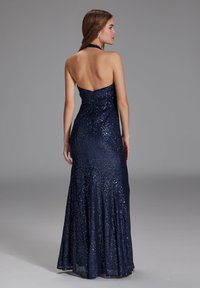 Navy sinivai sequin gãojék með hálsvöðvum og opnum baki, sem hefur fittan líkami og flæði pils sem breiðir úr sér frá hnjánum.