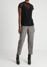 Black top with lace cap sleeves and round neckline, paired with gray plaid trousers and black pointed ankle boots.