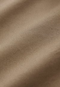 Tissu tissé beige avec texture visible et plis subtils créant des ombres douces et des reflets.