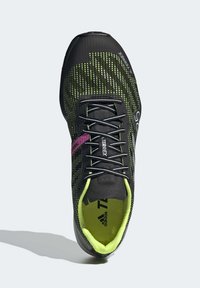 Czarno-zielony but sportowy z siateczkową cholewką, teksturowanym wykończeniem i fioletowym akcentem. Posiada sznurowaną konstrukcję oraz wyściełane wnętrze.