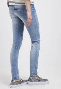 Světle modré skinny džíny s jemným odřením, roztržením na stehně, designem pěti kapes a klasickou denimovou texturou, doplněné šedými nazouvacími botami.