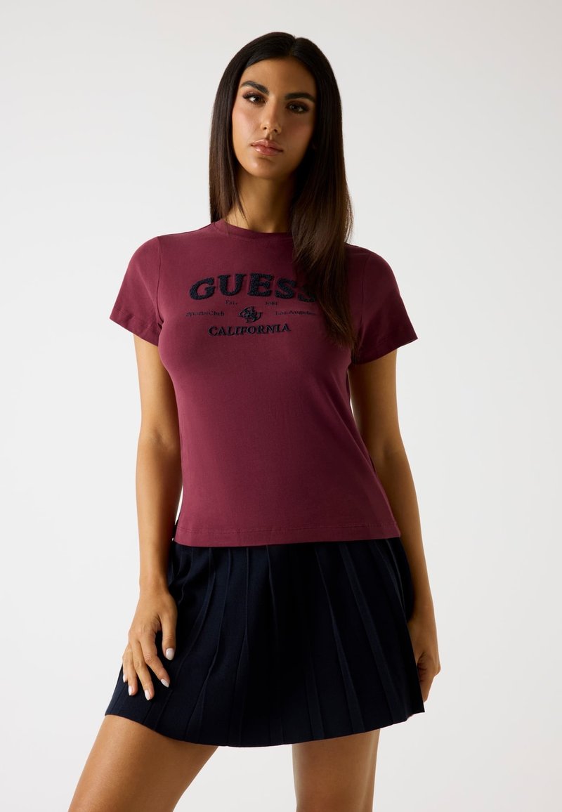 Burgundia puuvillane t-särk lühikeste varrukatega, millel on tikitud "GUESS CALIFORNIA" logo; koos plisseeritud tumesinise seelikuga.