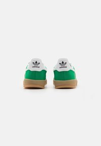 Zelené tenisky s hladkým syntetickým svrškem a bílými akcenty. Mají gumovou podrážku a černé logo adidas na patě.