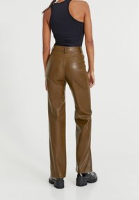 Pantalons taille haute en simili cuir marron avec une coupe droite, dotés de deux poches arrière et de détails de couture visibles.