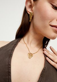 Juego de joyería en tono dorado que incluye pendientes en forma de alas y un collar con colgante de corazón, con detalles intrincados y un acabado suave y brillante.