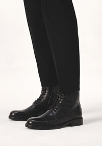 Bocanci negri din piele, cu vârful rotund, șireturi în față și fermoar pe lateral. Design minimalist cu o textură netedă și o talpă robustă.