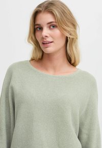 Maglione a maglia verde chiaro con scollatura rotonda, vestibilità rilassata e texture a costine fine. Il tessuto morbido cade dolcemente sul corpo.
