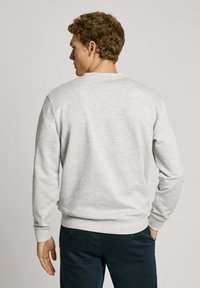 Sudadera gris de manga larga, cuello redondo, textura suave, con puños y dobladillo de canalé; llevada con pantalones oscuros.