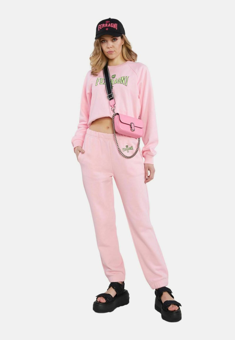 Rosa, kurz geschnittenes Sweatshirt und passende Jogginghose mit Logo-Details. Accessoires: eine rosa Umhängetasche und schwarze Plateausandalen.