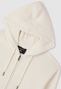 Felpa con zip color crema, dotata di cordini e etichetta nera con la taglia XL all'interno del collo.
