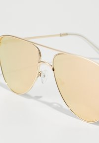 Occhiali da sole aviator dorati con lenti ambra tintate, dotati di una montatura in metallo, naselli regolabili e un design elegante.