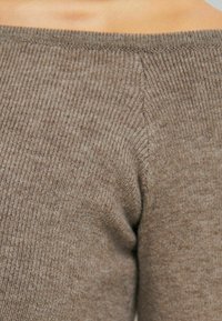 Jersey de punto marrón con textura acanalada y cuello off-the-shoulder. La textura del tejido parece suave con líneas verticales uniformes. Diseño minimalista.