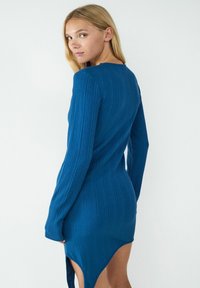 Langärmliges, geripptes Kleid in einem leuchtend blauen Farbton, mit asymmetrischem Saum und figurbetonendem Schnitt, aus weichem Stoff.