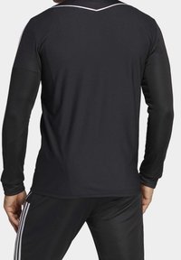 Camiseta deportiva negra de manga larga con tejido texturizado, detalles blancos en los hombros y un sutil detalle en forma de v en el escote.