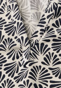 Tessuto di cotone con un motivo a foglie blu navy su uno sfondo chiaro. Caratterizzato da un design a V e da dettagli di cucitura ordinati.