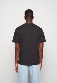 Svart bomull t-shirt med korta ärmar, något lös passform och rundad nederkant. Lappen synlig på den nedre sömmen. Bakifrån visas.