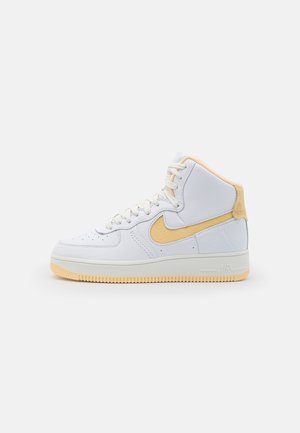 Baskets montantes blanches avec semelle beige, logo Nike beige et doublure de col beige, présentées sur un fond blanc uni.