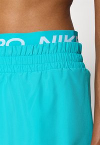 Akvově modré sportovní šortky mají nařasený elastický pas s bílým logem "NIKE". Materiál je hladký a lehký.