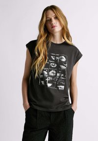 Camiseta de algodón negra sin mangas, con un estampado gráfico de labios en un patrón de cuadrícula. Ajuste ligeramente holgado que completa el look.