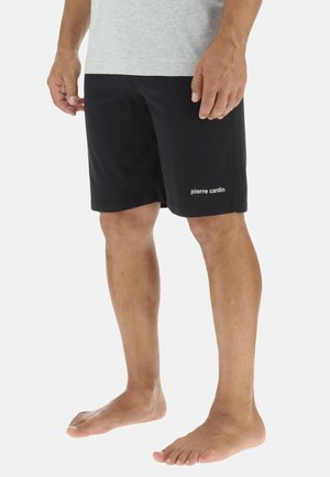 Shorts de sport noirs en tissu doux, avec des poches latérales et un logo blanc sur le bas à gauche. Design basique, coupe à mi-genoux.