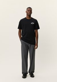 Μαύρο βαμβακερό μπλουζάκι με το λογότυπο "LES DEUX" στο στήθος, συνδυασμένο με γκρι παντελόνια ραμμένα στα μέτρα και μαύρα παπούτσια. Απλός σχεδιασμός, εφαρμοστή γραμμή.